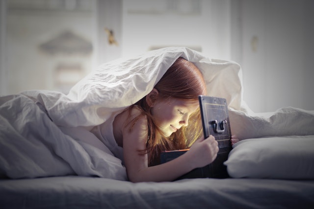 girl-lying-on-bed-looking-at-an-open-lighted-box-3887696